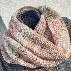 Op de afbeelding: Een zachte, roze, bruine en beige gebreide oneindige sjaal. De sjaal is dubbelgevouwen en over een mannequin gelegd.