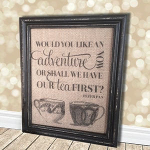 Peut inclure: Une impression sur toile de jute encadrée avec la citation "Voulez-vous une aventure maintenant ou devrions-nous prendre notre thé d'abord ?" de Peter Pan. L'impression présente deux illustrations en noir et blanc de tasses à thé.