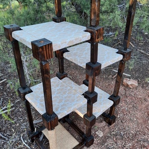 May include: A multi-level cat tree constructed from dark stained wooden posts and square frames. It features four platforms covered in a light beige fabric with a white geometric pattern and a base section wrapped in natural tan sisal rope.