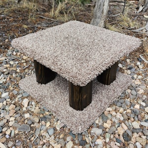 May include: A brown wooden cat scratching post with a beige carpet covering the top and base. The post is designed with two platforms for cats to climb on.