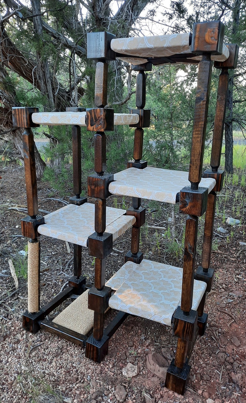 May include: A multi-level cat tree constructed from dark stained wood posts and square blocks. It features four platforms covered in a light beige fabric with a white geometric pattern, a vertical sisal rope scratching post, and a base with sisal matting.