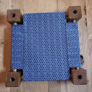 May include: A small pet bed featuring a rectangular blue fabric panel with a repeating white geometric pattern. The fabric is suspended between four square, dark brown wooden corner posts, each with a circular hole drilled into the top surface.