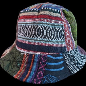 May include: A bucket hat constructed from various patchwork fabric panels featuring a mix of woven textures and patterns. The design incorporates stripes, geometric shapes, and floral motifs in a palette of red, blue, green, black, and white.