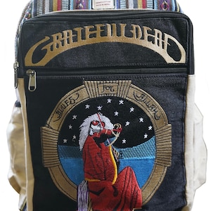May include: A backpack with a black front panel featuring an embroidered design of a skeleton playing a violin, with the words "Grateful Dead" above. The top section has a colorful striped pattern, and the sides are beige.