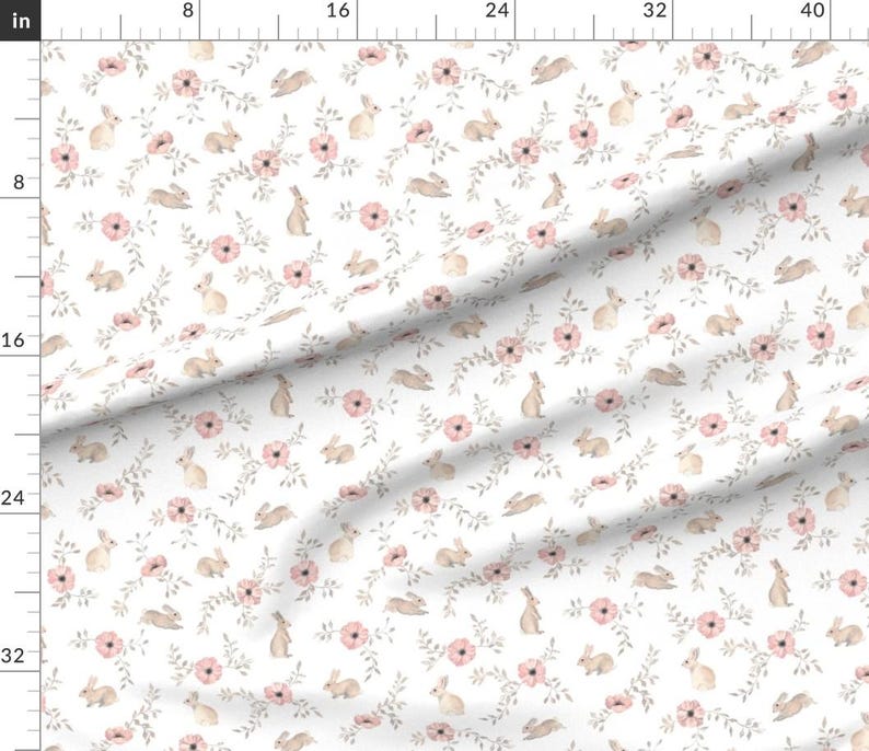 May include: White fabric with a repeating pattern of light brown bunnies, pink flowers, and gray-green leaves. The bunnies are in various poses, and the flowers have multiple petals. The overall design is delicate and floral.