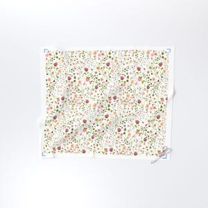 May include: A white fabric with a delicate floral pattern. The design features a repeating pattern of small flowers in shades of pink, purple, and yellow, along with green leaves and stems. The overall effect is a soft, watercolor-like aesthetic.