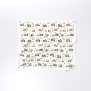 May include: White fabric with a repeating pattern of watercolor mountains, suns, clouds, and trees in muted colors. The text "ADVENTURE AWAITS" is printed throughout the design. The fabric is folded and has a pair of scissors in the corner.