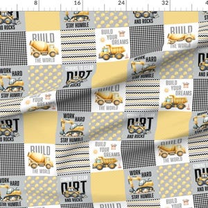 May include: Fabric with a patchwork design featuring construction vehicles like cement mixers and dump trucks. The squares alternate between yellow, gray, and black and white patterns. Text includes "Build Your Dreams" and "Work Hard."