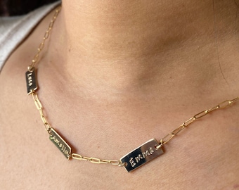 May include: A gold chain necklace with four rectangular name tags. The names on the tags are "Emma", "Amelia", "Lola", and "Ava".
