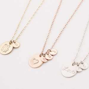 May include: Three gold necklaces with different charms. The first necklace has a charm with an angel holding a baby, the second necklace has a charm with a heart, and the third necklace has a charm with the word "Love".