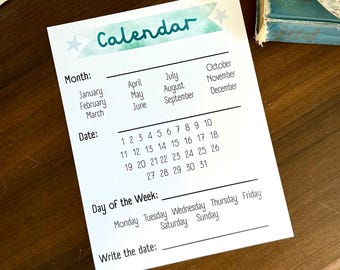 May include: A white calendar with the word "Calendar" in teal script. The calendar includes sections for the month, date, day of the week, and a space to write the date. The calendar is on a dark wooden surface.