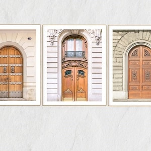 May include: Three framed prints of ornate wooden doors with arched entryways. The doors are all different styles, with one featuring a carved design, one with a simple panel design, and one with a more elaborate design. The prints are all in a white frame.