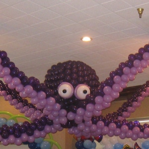 May include: A purple and white balloon octopus with eight tentacles hanging from the ceiling. The octopus is decorated with two large, white eyes. Two gold chandeliers hang from the ceiling above the octopus.