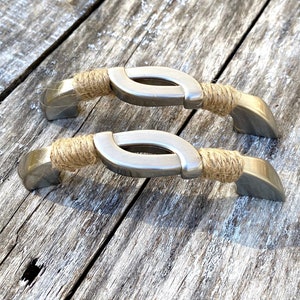May include: Two silver cabinet pulls with a rope-like design. The pulls have a curved shape and are wrapped with natural twine.