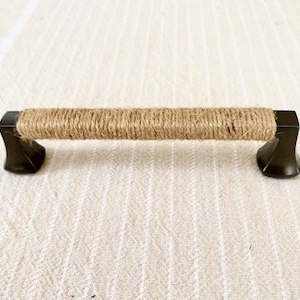 May include: A black metal cabinet pull with a brown jute rope wrapped around the center.