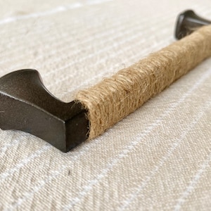 May include: A dark brown metal cabinet pull with a natural jute rope wrapped around the handle.