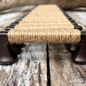 May include: A set of brown metal drawer pulls with a natural jute rope wrapped around them. The pulls are arranged in a row on a wooden surface.
