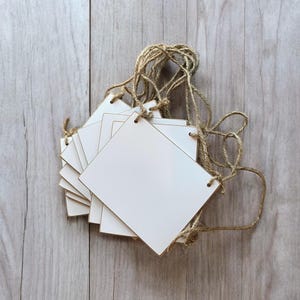 May include: A set of blank white wooden square signs with a gold trim, strung together with twine. The signs are perfect for adding a personalized touch to any event or home decor.