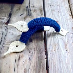 May include: A pair of blue rope cabinet pulls with white ceramic ends. The pulls are tied in a knot and have a rustic look.