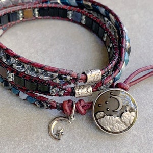 Può includere: Un braccialetto multistrato con cordoncino in pelle rosso scuro e perline nere e argentate. Il braccialetto ha un ciondolo argentato con una luna crescente e nuvole.