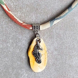 May include: A fabric necklace with a colorful patterned design and a pendant featuring a seashell with a silver seahorse charm.