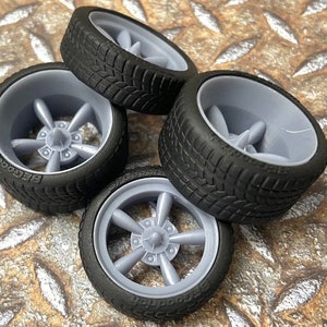 Puede incluir: Cuatro ruedas de coche modelo negras y grises con un diseño de cinco radios. Las ruedas son de goma y tienen un dibujo de la banda de rodadura.
