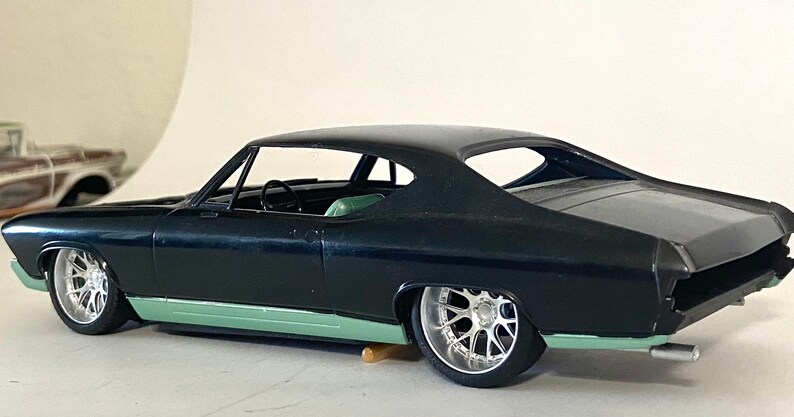 Puede incluir: Un coche modelo negro con un chasis verde y grandes ruedas plateadas. El coche es un Chevrolet Chevelle de 1967.