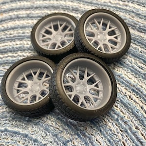 Puede incluir: Cuatro ruedas de coche modelo grises y negras con un dise&ntilde;o de radios. Las ruedas est&aacute;n sobre una superficie texturizada azul y blanca.