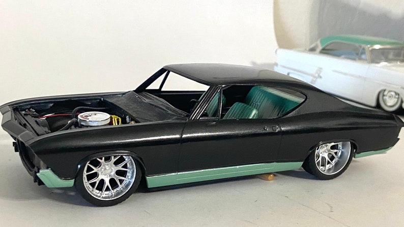 Puede incluir: Un coche modelo negro con el cap&oacute; abierto, que revela el motor. El coche tiene un interior verde y ruedas plateadas.