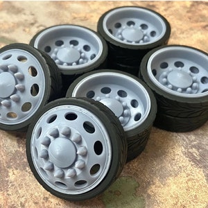 May include: Six gray and black truck wheels with a detailed tread pattern. The wheels have a silver rim and a gray center cap with a raised design.
