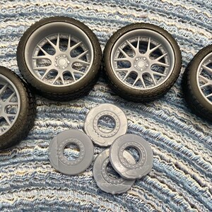 Puede incluir: Cuatro ruedas de coche modelo grises y negras con un dise&ntilde;o de radios plateados. Tambi&eacute;n se incluyen cuatro rotores de freno de pl&aacute;stico grises.