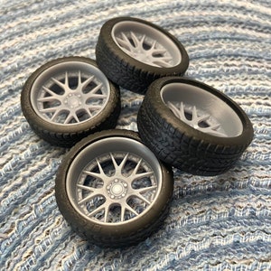 Puede incluir: Cuatro neum&aacute;ticos de caucho negro con llantas grises de radios detallados. Los neum&aacute;ticos est&aacute;n dispuestos en una pila sobre una superficie con un patr&oacute;n azul y blanco.