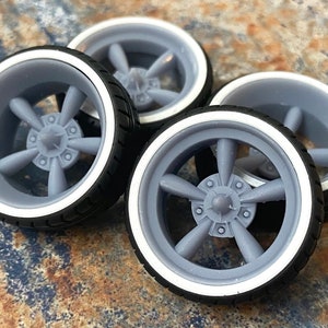 May include: Four gray plastic model car wheels with whitewall tires. The wheels have a five-spoke design.