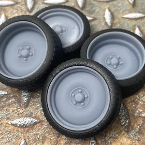 May include: Four gray rubber tire molds for model car wheels. The molds are made of a flexible rubber material and have a smooth, rounded surface.