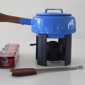 Pode incluir: Panela de fondue de esmalte azul com uma pega de madeira, um suporte de metal preto e quatro garfos de fondue com cabos coloridos.