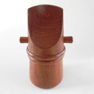 以下が含まれることがあります： 赤みがかった茶色の手作りの木製スクープ。スクープは、湾曲したハンドルと円筒形のベースを備え、中央に装飾的なリングが付いています。2つの小さな木製のペグが側面から伸びています。