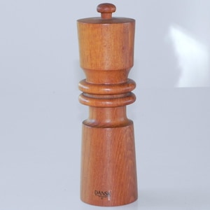 Może przedstawiać: Drewniany młynek do soli i pieprzu o prostym designie. Młynek wykonany jest z naturalnego drewna i ma ciemnobrązowy kolor. Nazwa marki "DANSK" jest nadrukowana na spodzie młynka.
