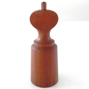 Może przedstawiać: Drewniany młynek do pieprzu z cylindryczną podstawą i zaokrągloną górą. Młynek wykonany jest z ciepłego, czerwonobrązowego drewna i ma gładkie, wypolerowane wykończenie. Na górze znajduje się mały, cylindryczny uchwyt.