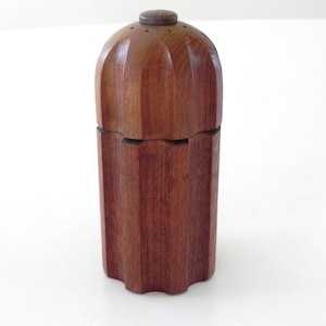 Może przedstawiać: Ręcznie wykonany drewniany pojemnik z pokrywką. Pojemnik ma ciepły brązowy kolor i cylindryczny kształt z pionowymi rowkami. Pokrywka jest zaokrąglona i ma mały, okrągły guzik na górze. Pojemnik jest prawdopodobnie używany do przechowywania.