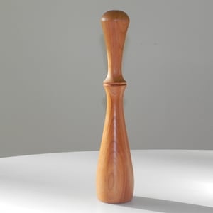 Może przedstawiać: Drewniany tłuczek z zaokrąglonym wierzchołkiem i smukłym, zwężającym się korpusem. Tłuczek wykonany jest z jasnobrązowego drewna z naturalnym usłojeniem.