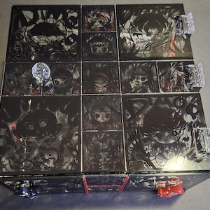 May include: A black wooden box with a glass top. The glass top is divided into nine squares, each with a different image of a cartoon character. The box is decorated with red and black accents. The box is closed and the glass top is reflecting light.