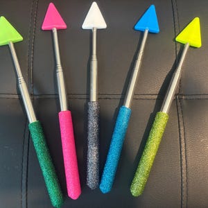 May include: Five telescopic tools with triangular heads in different colors: green, pink, white, blue, and yellow. The tools have a silver metal shaft and a glittery finish.