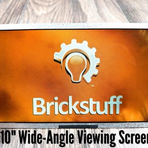 May include: A 10-inch wide-angle viewing screen featuring a rectangular display with a metallic frame. The screen shows an orange background with a white gear-shaped lightbulb icon and the text Brickstuff in white lettering.