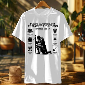 May include: White t-shirt featuring a black and white illustration of a kneeling knight holding a sword. The shirt includes text in Spanish: "PONTE LA COMPLETA ARMADURA DE DIOS EFESIOS 6:10-17" and various symbols representing elements of faith.