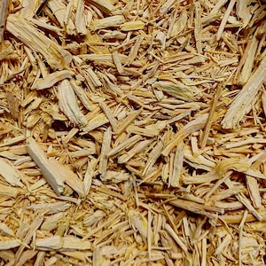 May include: Close-up of a pile of light brown wood chips. The chips vary in size and shape, with some appearing long and thin, while others are chunkier. The texture is rough and natural, suggesting a product for gardening or landscaping.