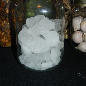 May include: A glass jar filled with clear, white rock candy. The jar is sitting on a black surface.