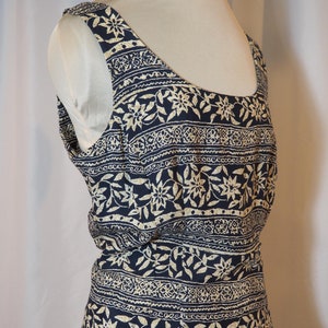 Puede incluir: Un vestido sin mangas con fondo azul marino y estampado floral blanco. El vestido tiene un escote redondo y un corpiño ajustado. La falda es amplia y fluida.