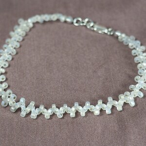 May include: A white beaded necklace with a silver clasp. The beads are arranged in a zig-zag pattern.