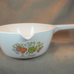 May include: White ceramic saucepan with a green, yellow, orange, and brown floral design featuring peppers, herbs, and the text "La Sauco".