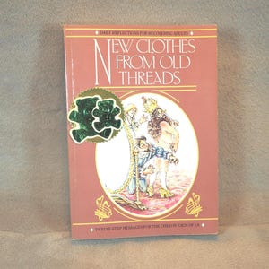 May include: A pink book with the title "New Clothes From Old Threads" and a green teddy bear sticker. The book is about daily reflections for recovering adults and twelve-step messages for the child in each of us.